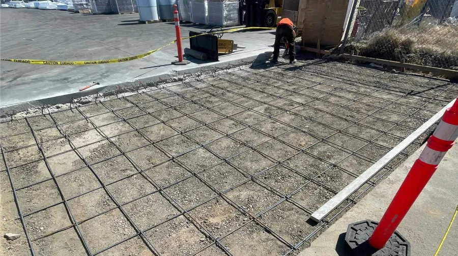 Construction worker preparing rebar grid for concrete pour at an industrial storage yard